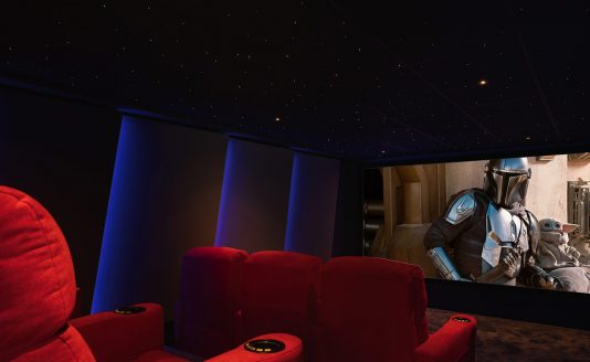 View of the cinema room from a red chair with a movie screening featuring yoda